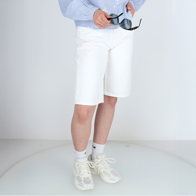 Eine Frau mit weißen Shorts, Sneakers und einer Brille in der Hand