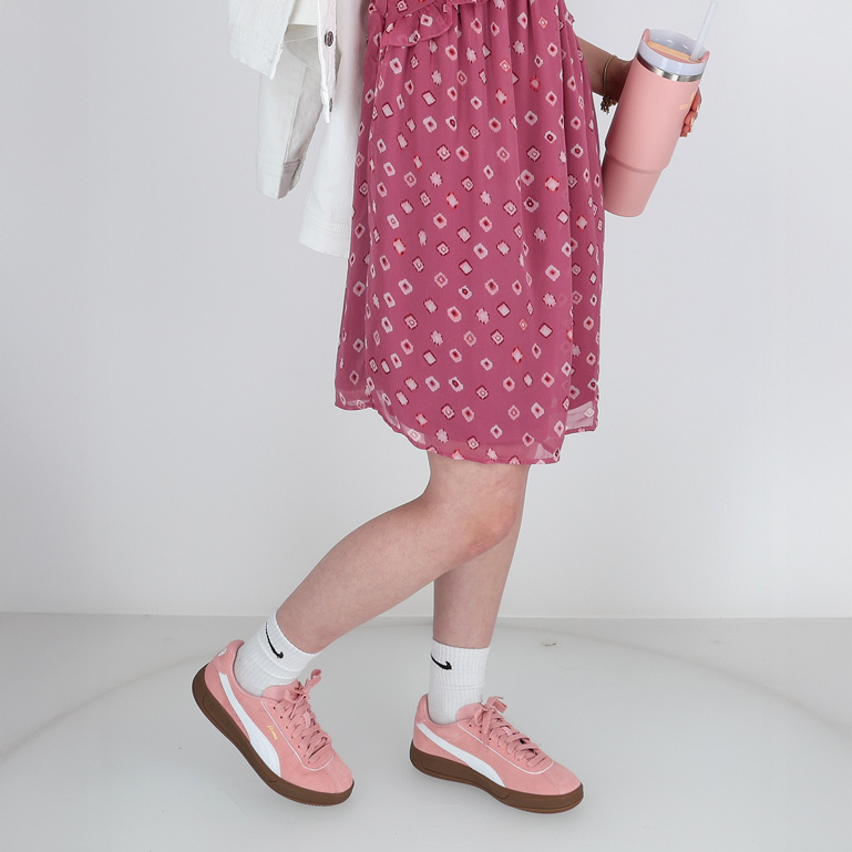 Frau im rosa Kleid, Sneakers und mit einem Trinkbecher in der Hand