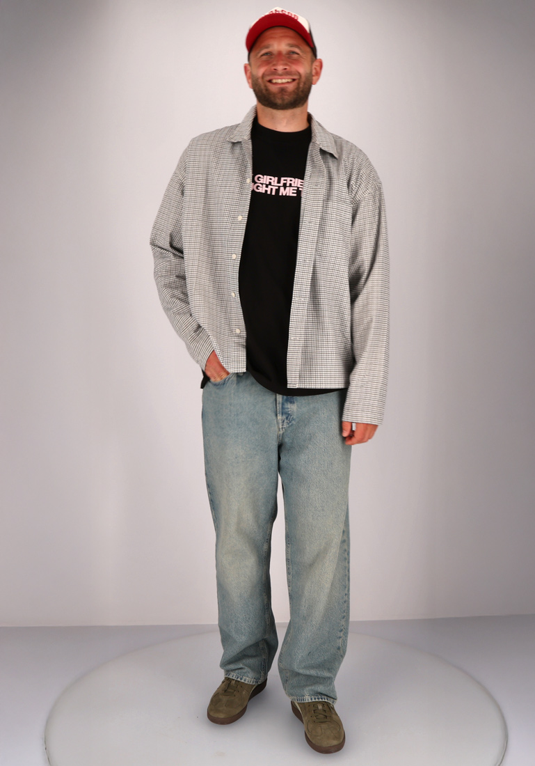 Ein Mann in einem karierten Hemd, Jeans, einer Basecap und Sneakers