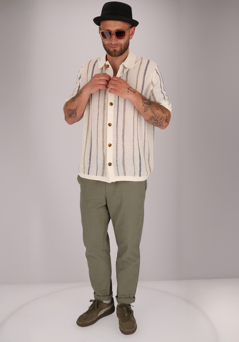 Ein Mann mit Hut, Brille und gestreiftem Hemd, der eine grüne Hose trägt