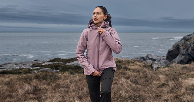 Frau zieht sich eine rosande Windjacke an und steht am Meer