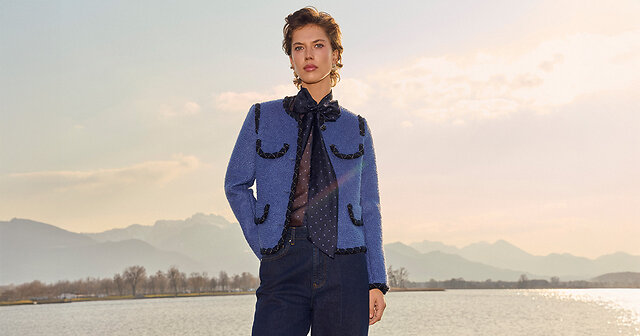 Frau steht vor einem See im schicken blauen Outfit