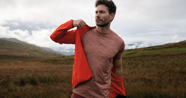 Wanderer zieht sich seine rote Funktionsjacke über ein atmungsaktives Shirt