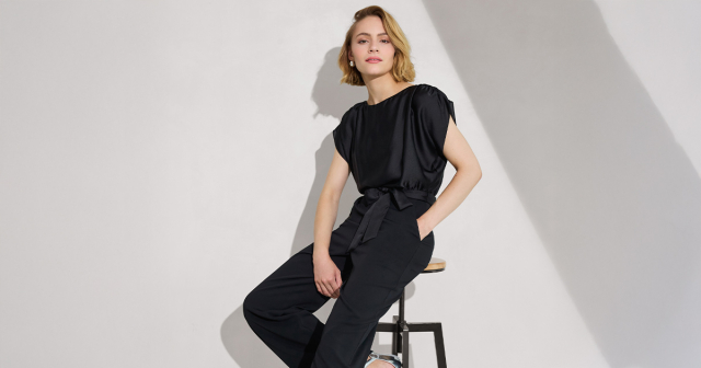 Frau in schwarzem Jumpsuit auf einem Stuhl