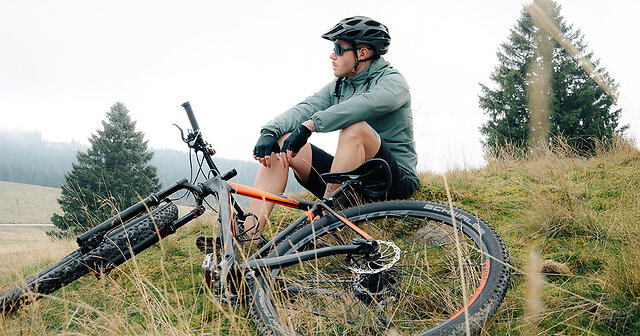 Mann sitzt mit seinem Fahrrad auf einem Hügel