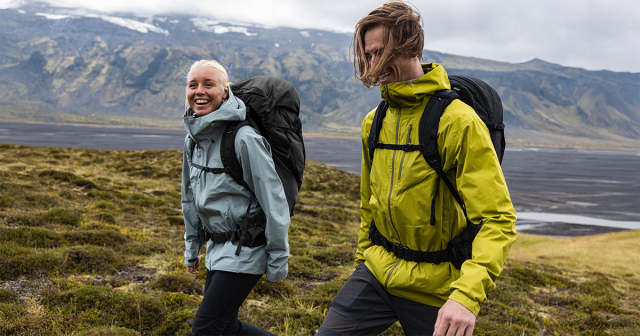 Frau und Mann wandern in einer grünen Windjacke und Wanderrucksack
