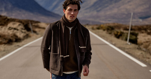Mann in brauner Jacke und braunem Schal steht auf einer Straße