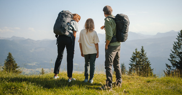 Familie steht von hinten beim Wandern auf einem Berg und schauen in die Ferne